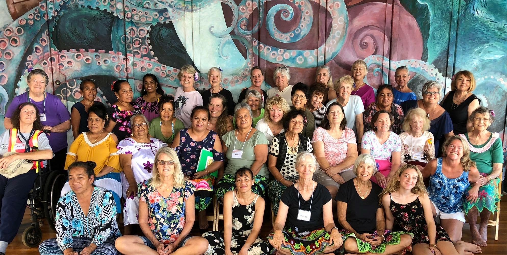 Diverse group of women smile in front of a mural at Camp Mokuleia