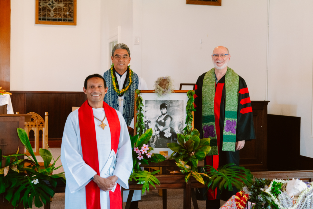Brandon Duran, Wendell Davis, David Popham stand around framed photo of Queen Liliuokalani at Soldiers Chapel for her birthday celebration in 2022