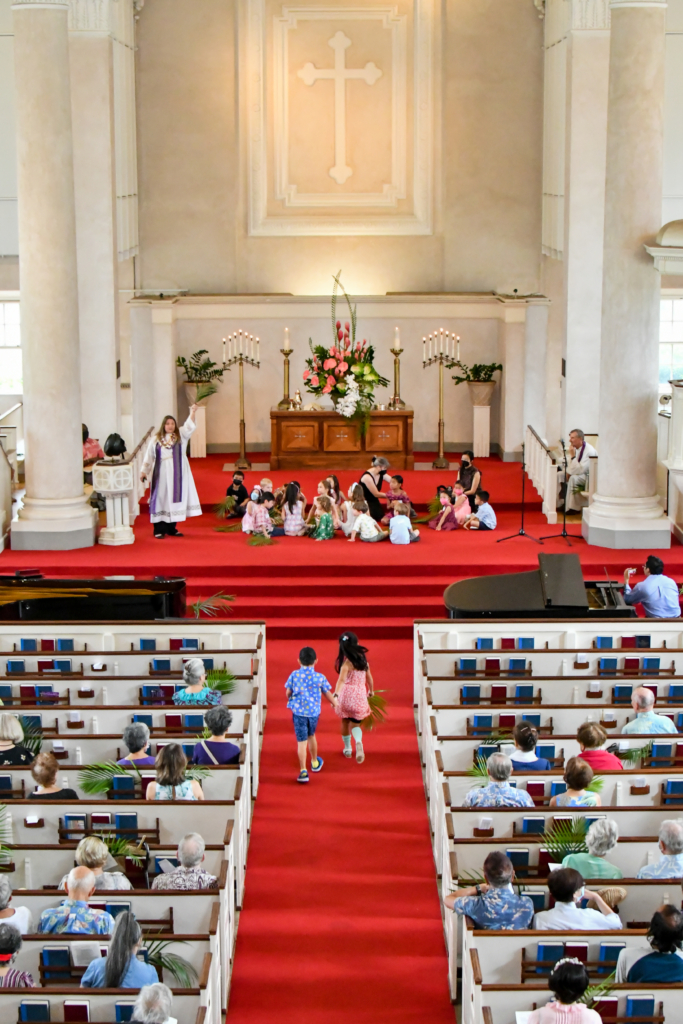 two children run side by side up to chancel steps where children are gathered for time with keiki in worship service