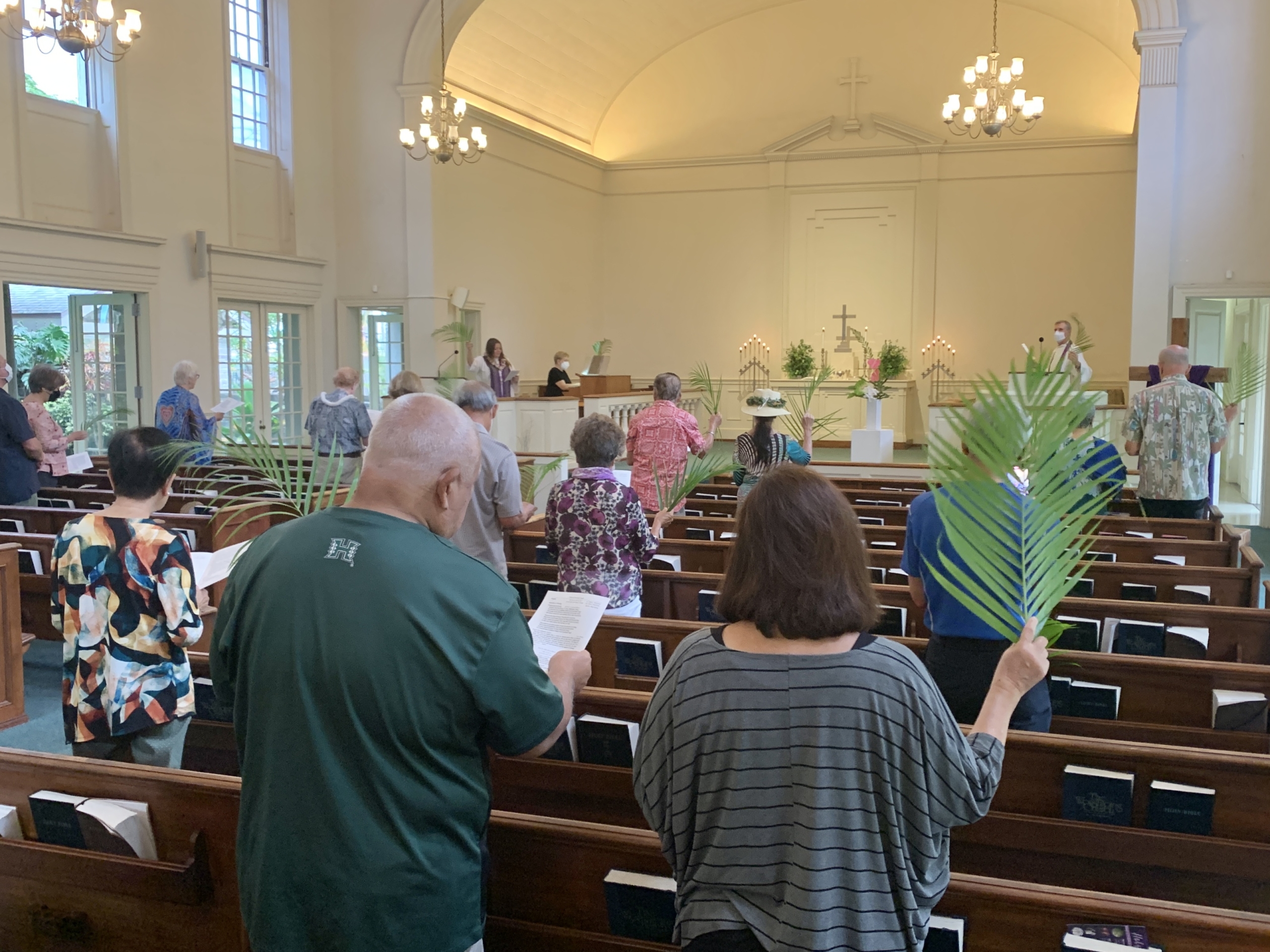people standing in pews during worship service holding palms on Palm Sunday