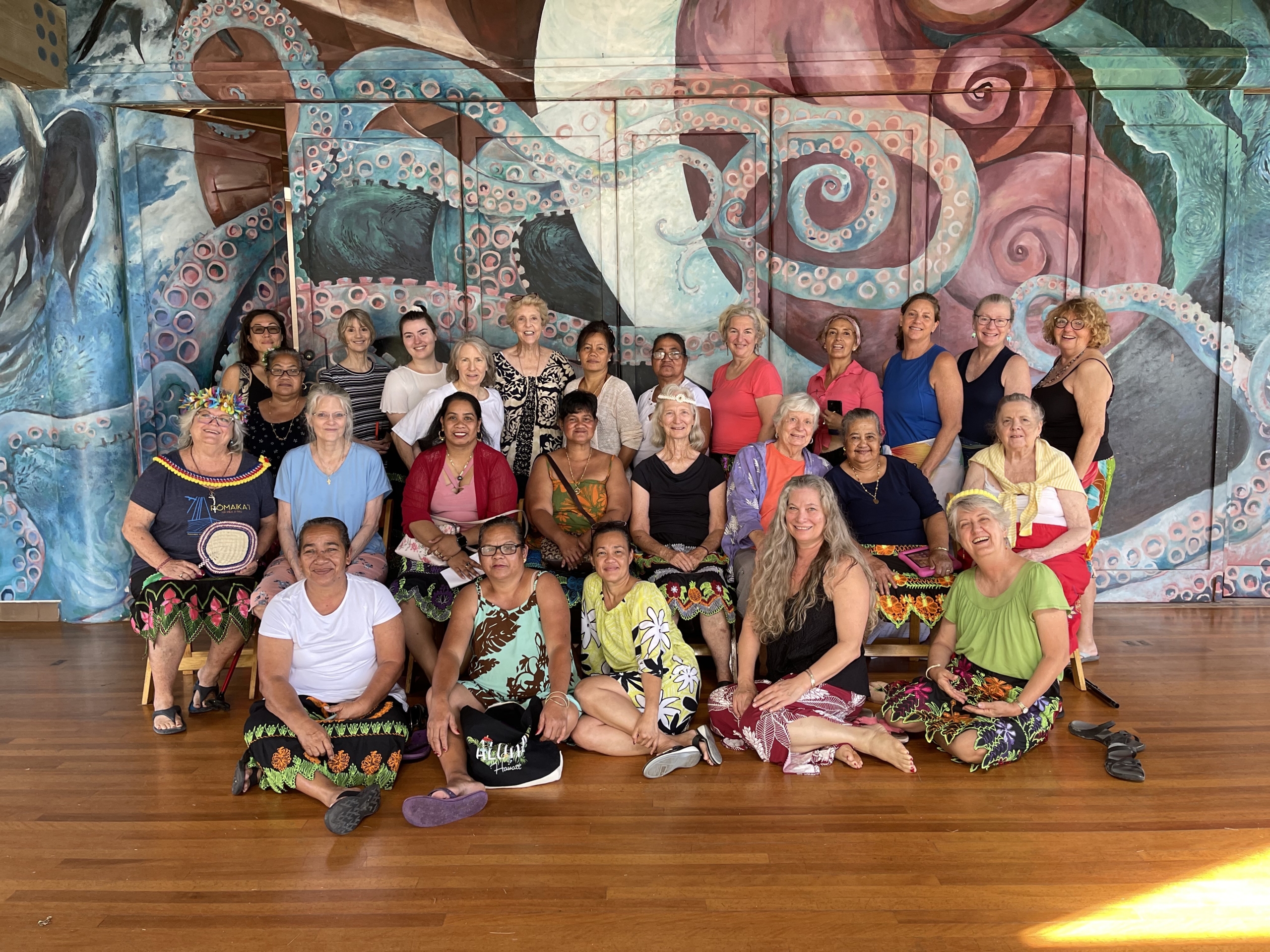 group of women smiling and sitting in front of mural at camp mokuleia chapel